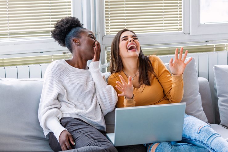 two women laughing together while on a laptop