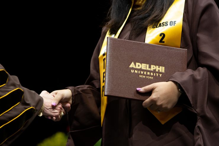 Graduate holding diploma while shaking hands during ӰƬ University graduation ceremony