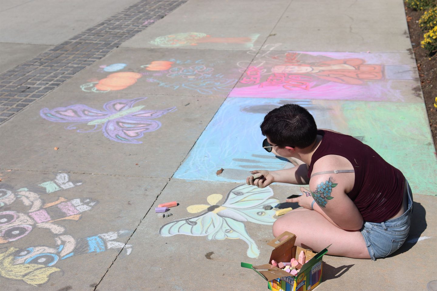 ӰƬ student draws butterflies on the sidewalk during Fall Arts Festival.