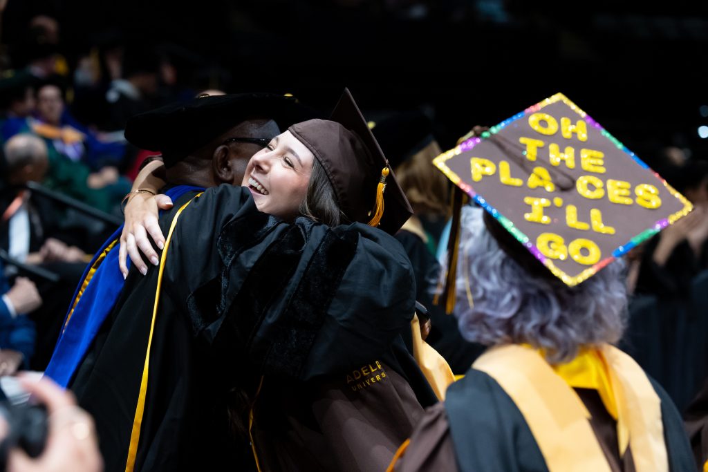 An ӰƬ University graduate in cap and gown hugs her professor during the commencement ceremony.
