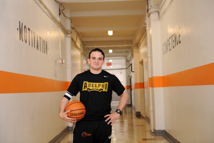 An ӰƬ alumni standing confidently in a hallway of a school holding a basketball.