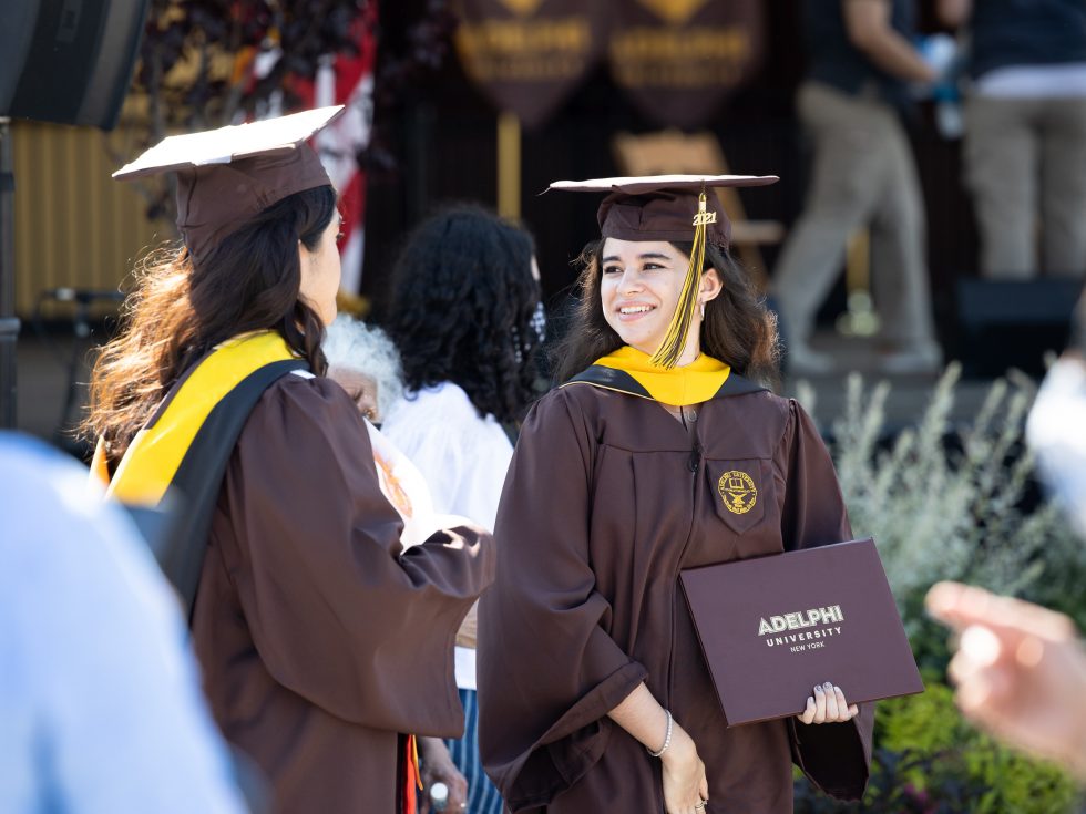 Two ӰƬ graduates holding diplomas and wearing regalia.
