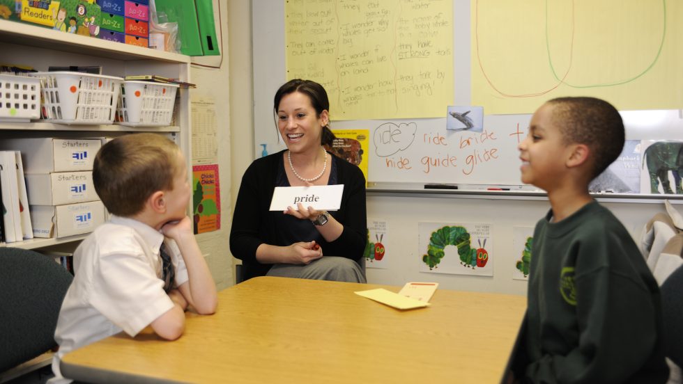 An ӰƬ student working with two school aged children on reading and speech skills with flash cards.