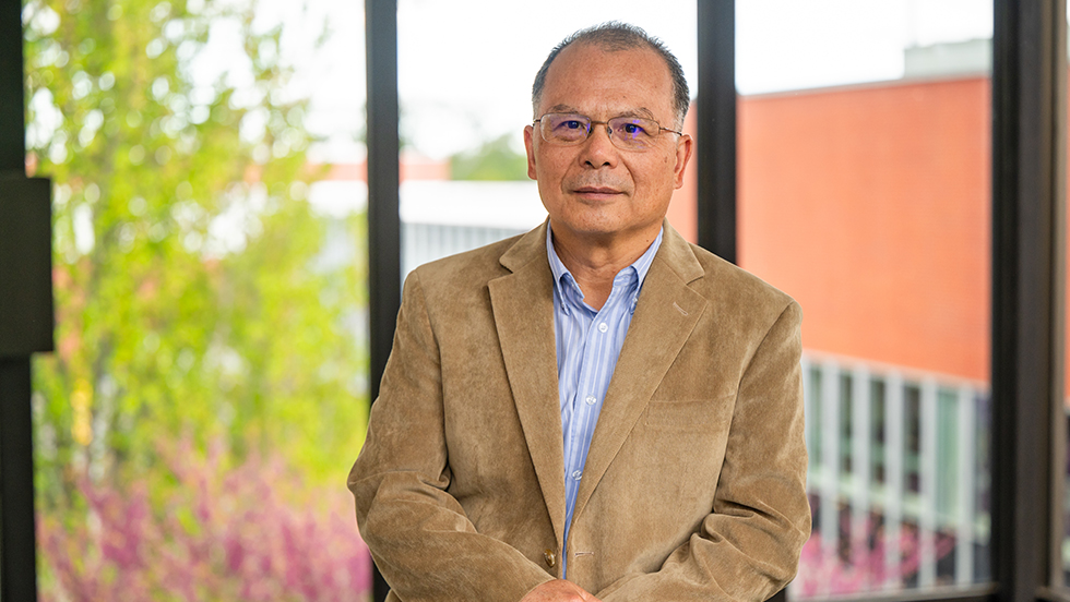  Dr. Huang facing the camera, standing in front of windows overlooking ӰƬ's campus.