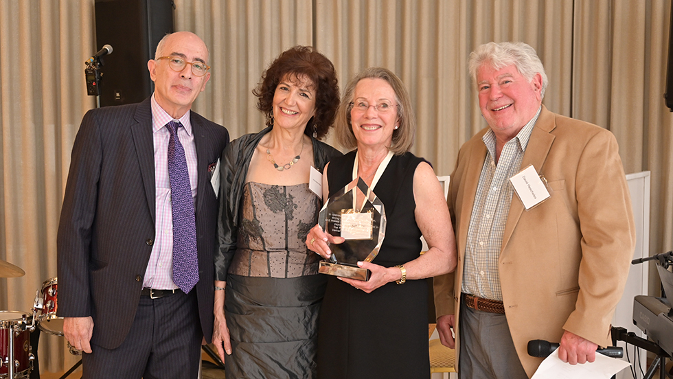 Three faculty members and a former student, all wearing party attire, stand for a photo. Mary Beth Cresci, who was honored at the gala, holds a glass plaque.